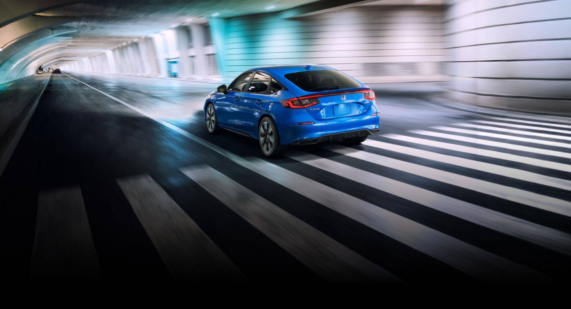 Honda Civic Hatchback Sport Touring Hybrid 2025 en Boost Blue Pearl conduciendo por un túnel subterráneo.