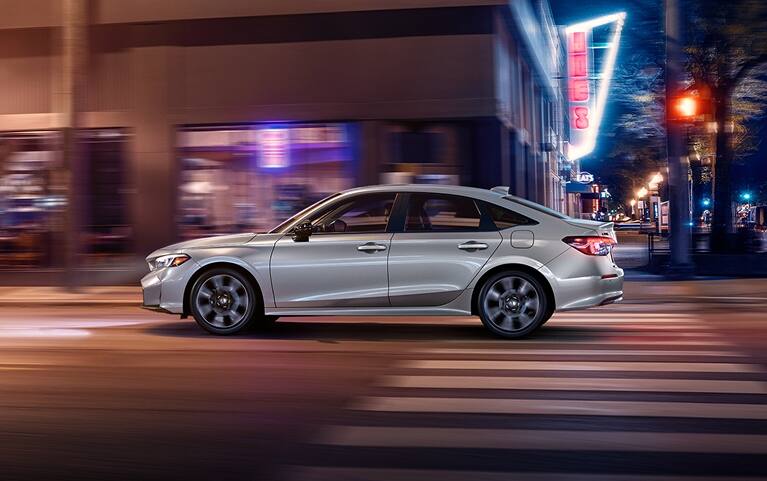 2027 Honda Civic Sedan Sport Touring Hybrid in Solar Silver Metallic side profile driving on a city street (Compact Sedan)